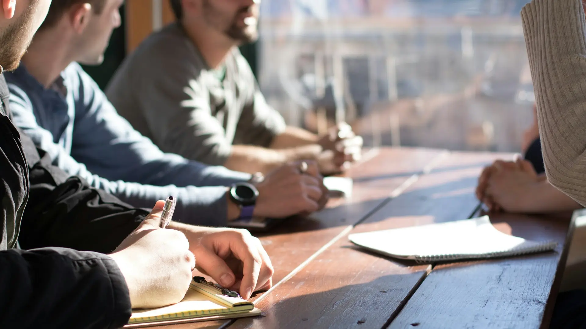 people sitting on chair in front of table while holding pens during daytime